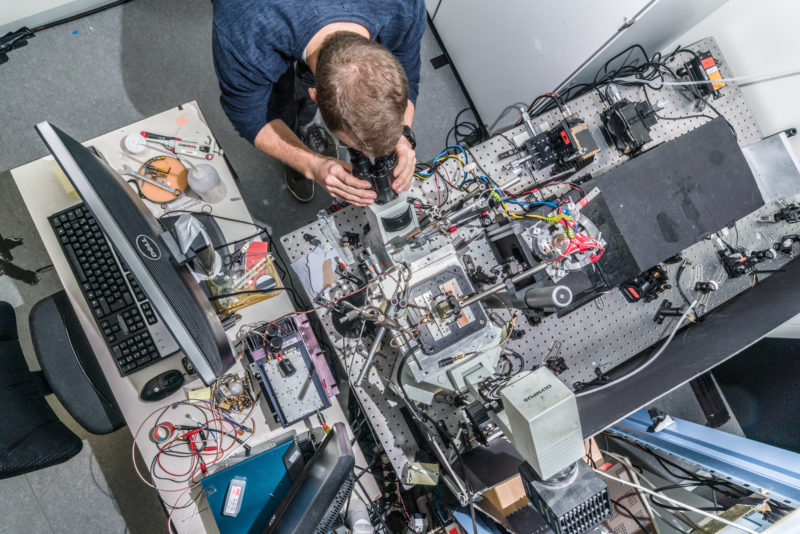 Wissenschaftsfotografie an einem Physikalischen Institut der Universität Stuttgart: Von oben fotografierter komplizierter Versuchsaufbau mit Forscher am 3. Physikalischen Institut der Universität Stuttgart.