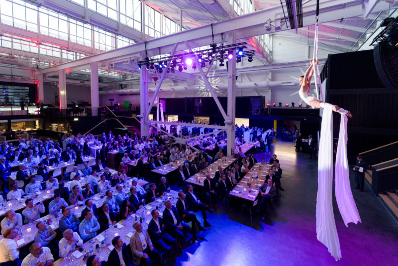 Editorial photography as event photography and fair photography: An acrobat is dancing on a cloth hanging from the ceiling at a company event.