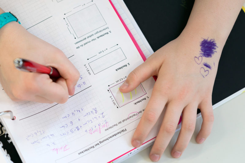 Reportagefotografie zum Thema Lernen und Bildung: Blick in ein Arbeitsheft einer Schülerin während des Geometrie-Unterrichts. Auf Ihrem Arm hat sie mit Kugelschreiber Herzen gemalt und daneben etwas durchgestrichen.