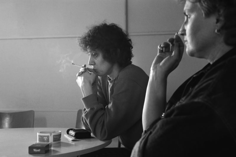 Schwarz-Weiss-Reportagefotografie an verschiedenen Arbeitsplätzen Anfang der neunziger Jahre: Zwei erschöpfte Näherinnen sitzen in ihrer Pause im Raucherzimmer einer der letzten deutschen Textilfabriken.