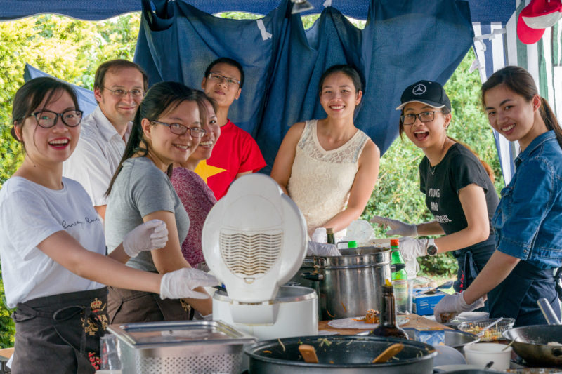 Reportagefotografie als Eventfotografie und Messefotografie: Asiatische Studierende freuen sich auf einem Universitätsfest beim Kochen von Spezialitäten aus ihrer Heimat.