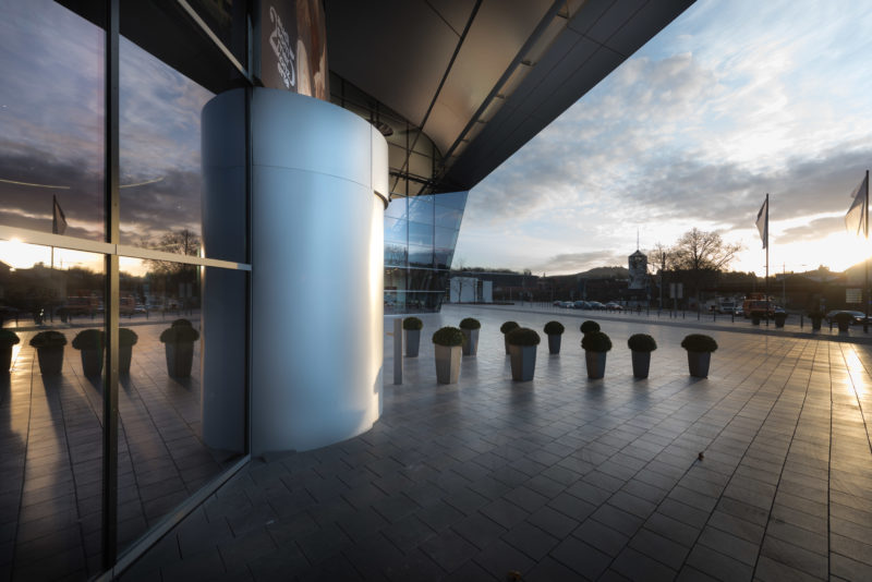 Architectural photography: Exterior view of an entrance area of a company at sunset. Plant tubs line the access path over the pavement of the forecourt.