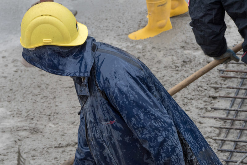 Reportagefotografie: Eine Betondecke wird gegossen. Die Arbeiter tragen Regenkleidung und Gummistiefel bei ihrer anstrengenden Arbeit.