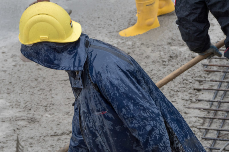 Editorial photography: A concrete ceiling is poured. The workers wear rainwear and rubber boots during their strenuous work.