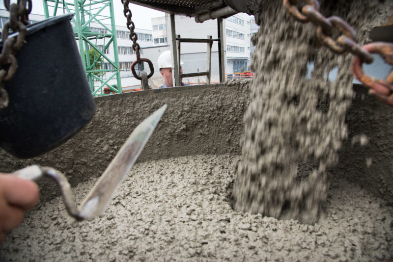 Reportagefotografie: Beton wird aus dem LKW in einen am Kran hängenden Betonkübel umgefüllt, der ihn dann zum Guss in die Verschalung bringt.