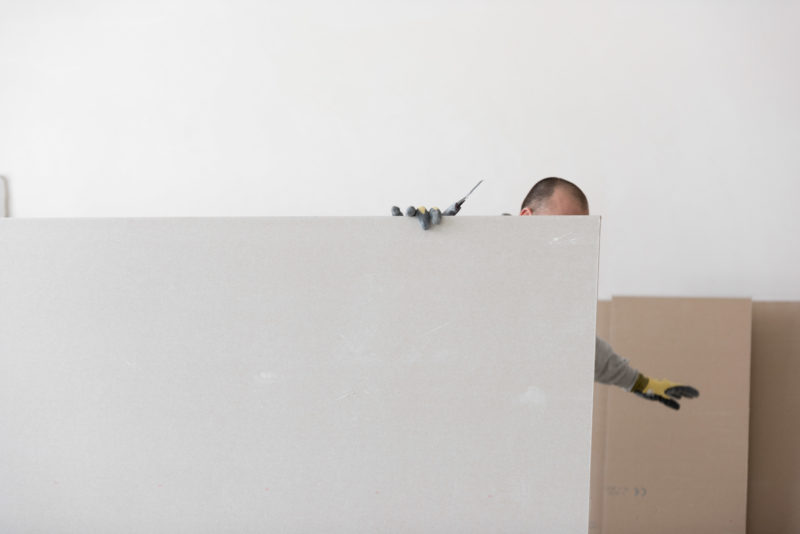 Editorial photography: During the interior work a worker cuts the plaster walls with a knife. He disappears behind the plasterboard, you can see his gloves and the knife.