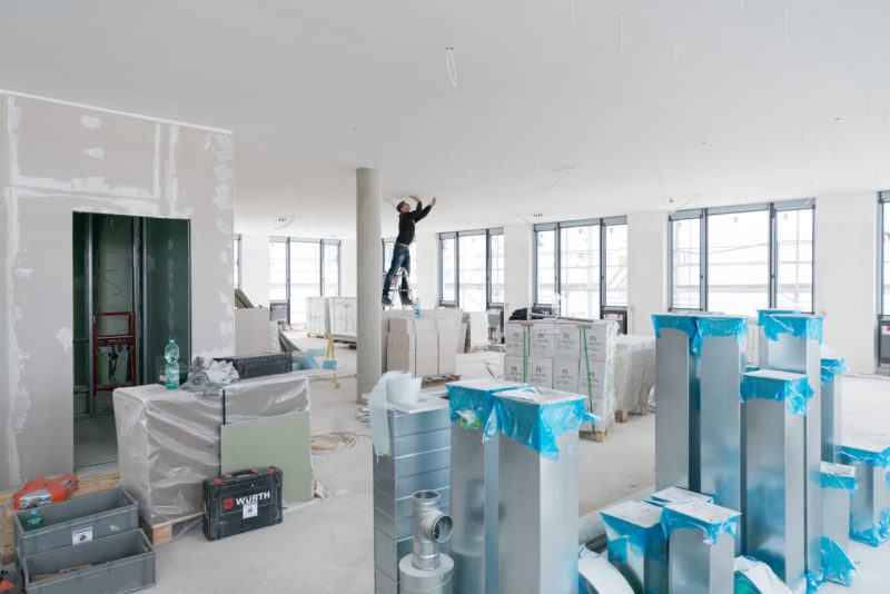 Editorial photography: On one floor there are a lot of materials that still need to be installed. A technician stands in between on a ladder and works on the ceiling.