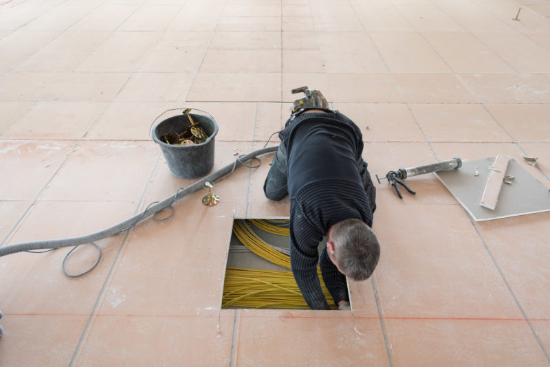 Editorial photography: An electrician reaches through a sawn opening into the cable intermediate floor.