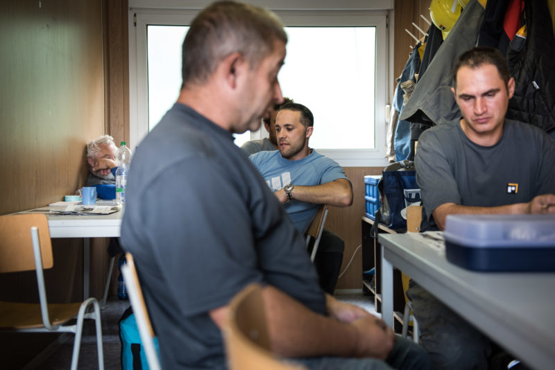 Reportagefotografie: Arbeiter sitzen in der ersten Pause am Morgen in einem Containerraum.