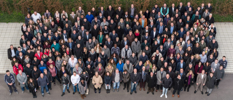 Gruppenfoto: Gruppenbild der gesamten Belegschaft einer Firma. Es wurde aus dem fünften Stock des Firmengebäudes aufgenommen und benötigte ein spezielles Seitenverhältnis für die Nutzung in einem Druckerzeugnis.