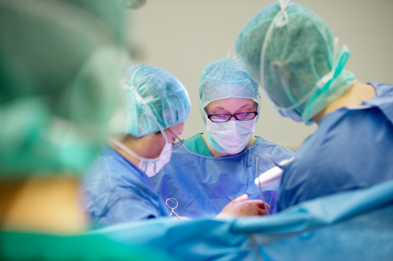 Healthcare photography: In the operating room, the surgeons stand next to each other at the table with the patient on it. It is important to have a good field of view on the use of the instruments.