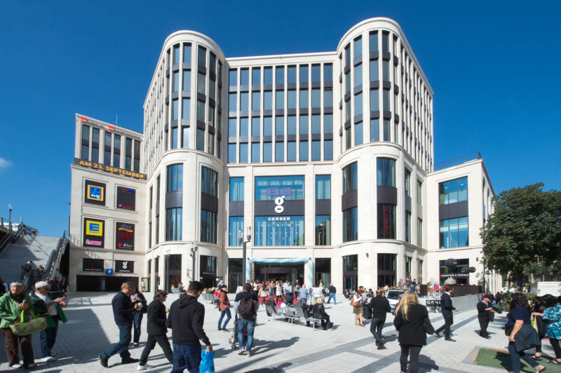 Architectural photography: Exterior view of Das Gerber, a new shopping centre in the centre of Stuttgart in the Gerberviertel. In good weather, many people populate the brightly paved square in front of it.