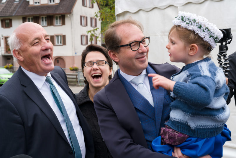 Editorial photography as event photography and fair photography: CSU politician Alexander Dobrindt visits an event in a small Bavarian town. A little girl in traditional costume is sitting on his arm.