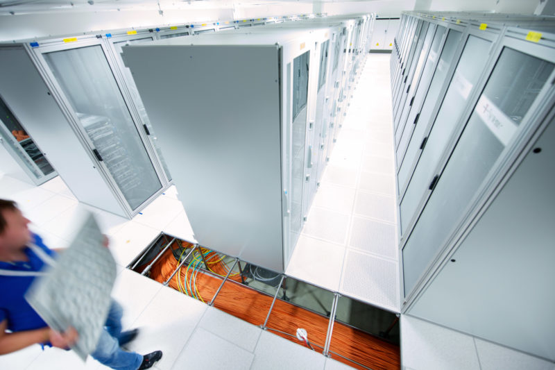 Industriefotografie: Ein Techniker öffnet in einem großen Serverraum den Doppeboden in dem sich große Kabelmengen befinden.