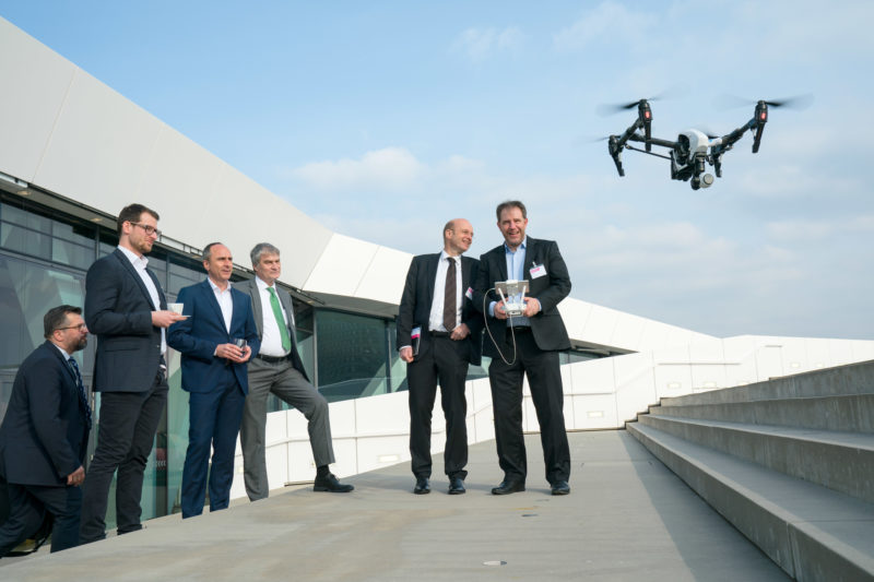 Editorial photography as event photography and fair photography: On the roof of the event location, participants of a company event observe the start of the demonstration of a professional camera drone.
