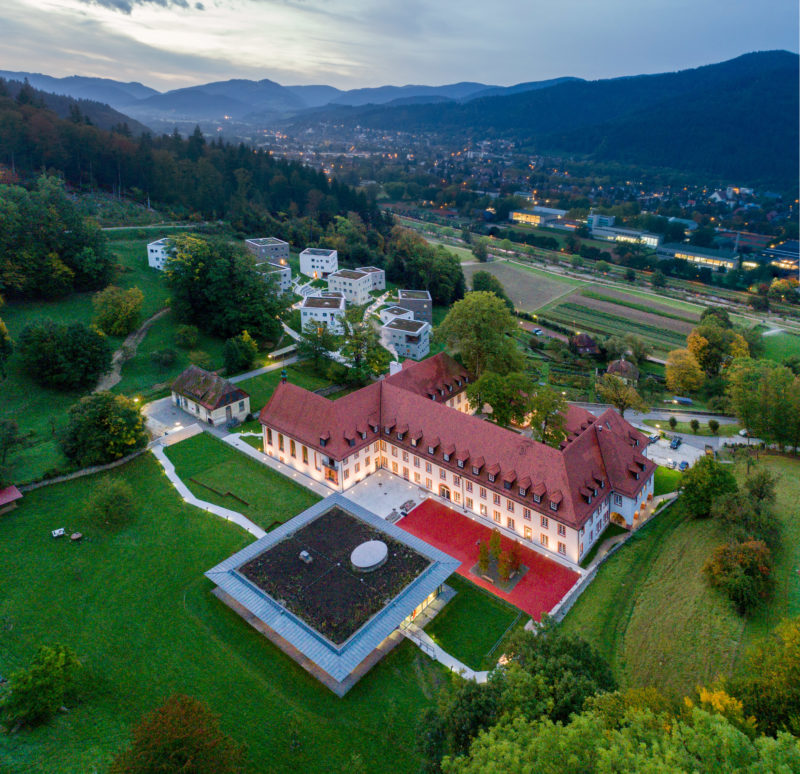 Luftaufnahmen und Drohnenfotografie: In Panoramatechnik fotografierte Drohnenaufnahme einer beleuchteten internationalen Schule bei einbrechender Nacht.