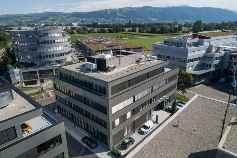 Luftaufnahmen und Drohnenfotografie: Ein neues Bürogebäude in einem Industriegebiet. Man sieht die schöne umgebende Berglandschaft.