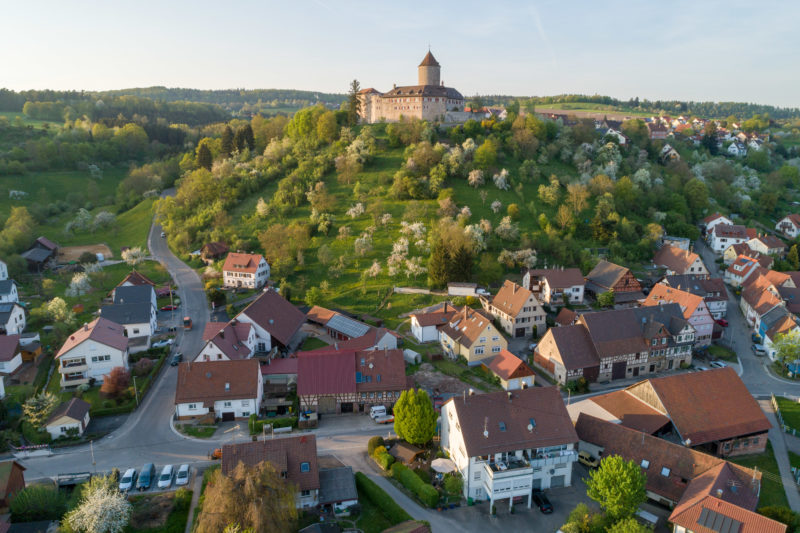 Landschaftsfotografie: Luftaufnahmen und Drohnenfotografie: Burg Reichenberg bei Oppenweiler im abendlichen Sonnenlicht. Blühende Obstbäume säumen den Burgberg, an dessen Fuss sich der Ort befindet.