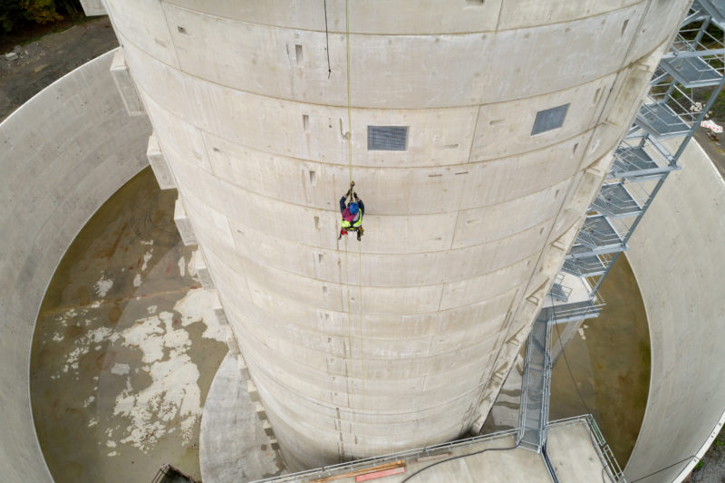 Luftaufnahmen und Drohnenfotografie: Ein Industriekletterer seilt sich von einem Windkraftwerksturm ab.