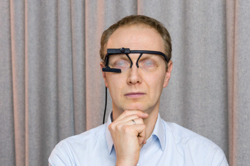 Editorial Photography: Scientist researches the interface between man and machine and the visual interaction required for this. In the portrait he wears glasses that record his eye movements. With long time exposure the eye movement becomes an interesting effect.