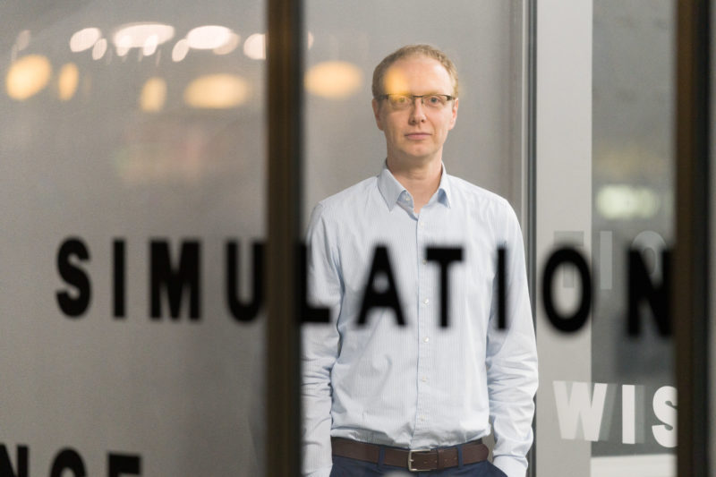 Editorial Photography: Scientist researches the interface between man and machine and the visual interaction required for this. The blurred writing at the entrance to the institute is a good foreground for another portrait photo of the scientist.