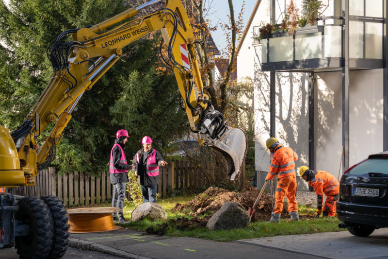 Reportage photography on a fiber optic construction site: An excavator supports the workers of the construction company digging a channel for the house connection with fiber optic cable.  