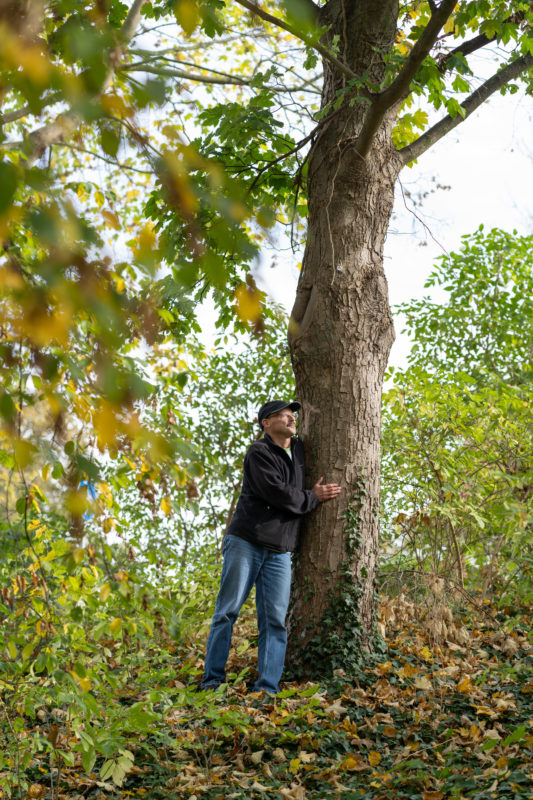 Editorial Portrait: Ein Liebhaber von Bäumen umfasst einen Baum in einem Stadtpark. Das Portrait wurde zur Unterstützung einer Baumpflanz-Initiative für ein Mitarbeitermagazin fotografiert.