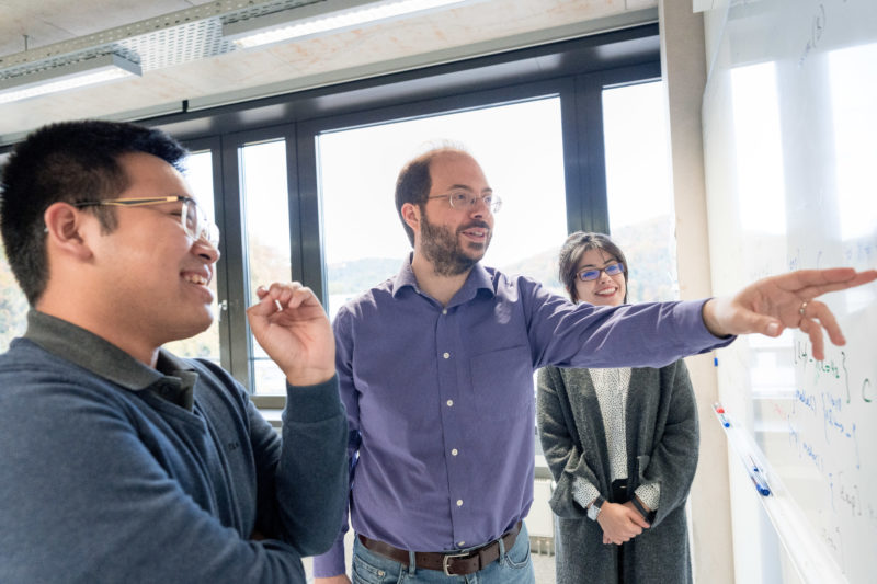 Portrait eines Wissenschaftlers: In eine abgerundete Portraitserie gehören auch Fotos der Menschen, die mit dem Abgebildeten in Beziehung sind. Hier ein Mitarbeiter und Mitarbeiterin mit dem Portraitierten am Whiteboard.