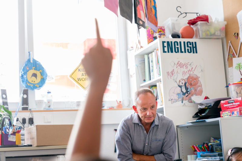 Editorial photography: An English teacher during class. He talks to the children and they give hand signals to answer his questions or to be allowed to say something.