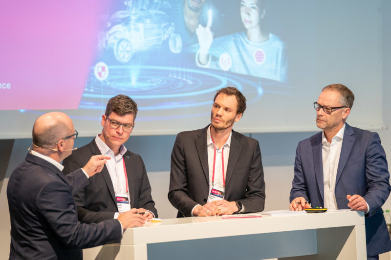 Eventfotografie: Eine Kundenveranstaltung eines IT-Unternehmens: Bei einem Podium kann der Moderator auch von hinten gezeigt werden, solange alle wichtigen Personen gemeinsam gut abgebildet sind.