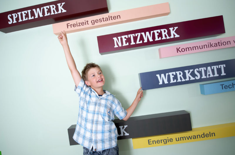 Editorial photography:  A pupil in an exhibition about science and research. He jumps enthusiastically into the air and points to the many signs that show the various offers in the exhibition.