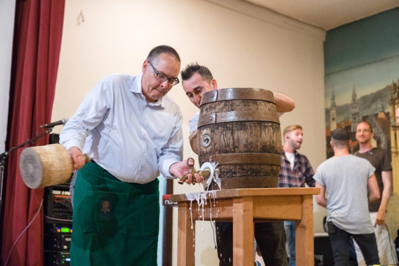 Reportagefotografie als Eventfotografie und Messefotografie: Fassanstich am Abend einer wissenschaftlichen Konferenz. Im Moment des ersten Schlages auf den Zapfhahn spritzt der Schaum aus dem Loch.