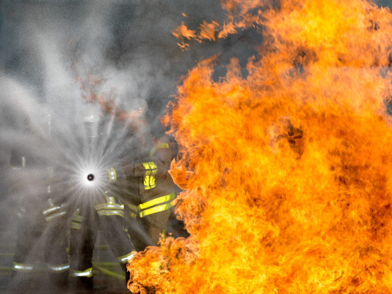 editorial photography: Three airport firemen hold a  fire hose nozzle into the blazing kerosene flames during an aircraft fire drill.