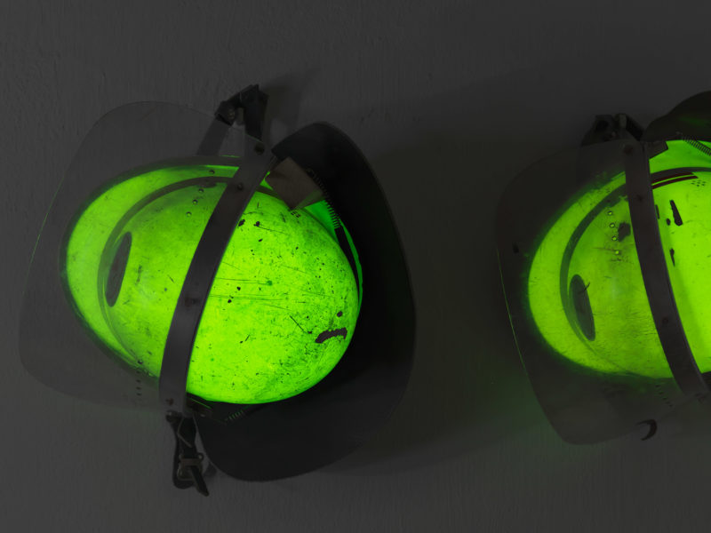 editorial photography: Firefighter helmets are hanging on a wall. They glow green in the dark. On the paint you can see the traces of past operations.