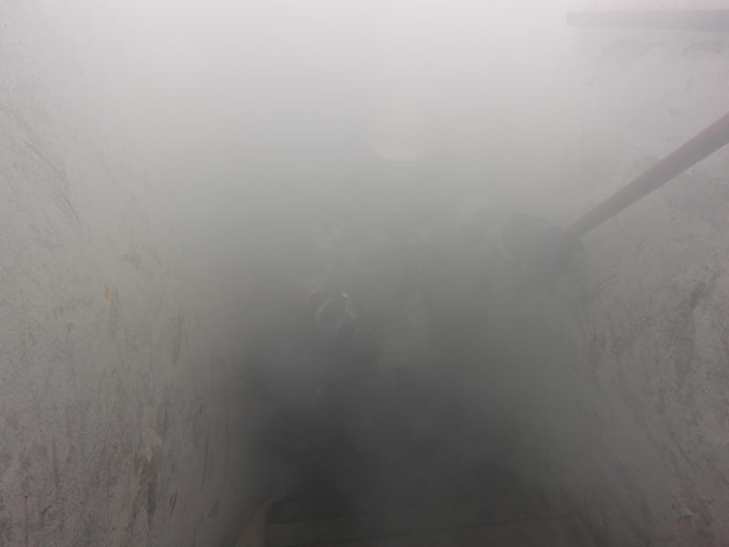 Reportagefotografie: Ein Feuerwehrmann geht durch den rauch in einem Kellerabgang. Man kann ihn kaum erkennen.
