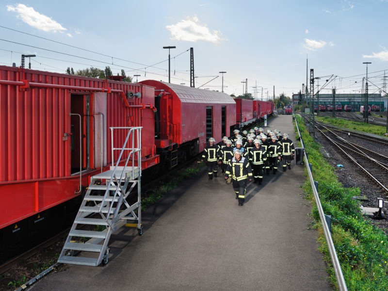 Reportagefotografie: Ein Trupp Feuerwehrleute geht zum Rettungszug, der bei einem Bahnunglück eingesetzt werden kann und insbesondere Einsätze in Tunneln erleichtern soll.