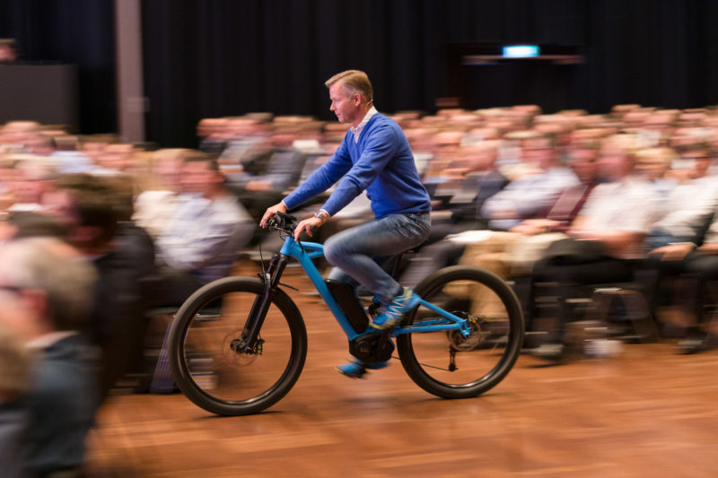 Editorial photography as event photography and fair photography: At a company event, an employee drives to the stage on an e-bike. The photo appears dynamic due to motion blur during the deliberately long shutter speed.