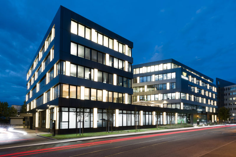 Architectural photography:  Long-term exposed night photograph of a brightly lit company building with the light tracks of passing cars in front of it.