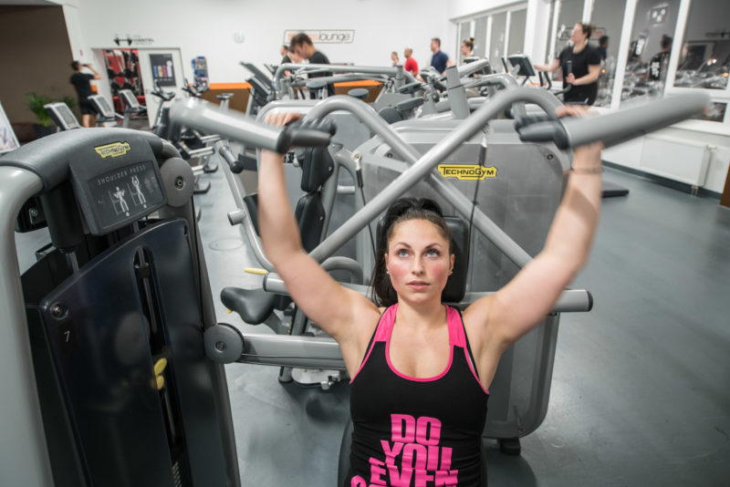 Mitarbeiterfotografie: Eine Frau trainiert in ihrer Freizeit im Fitnessstudio Ihre Armmuskeln.