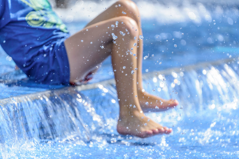 Feet of a boy playing in a shallow well. Drops of water splash through the air.