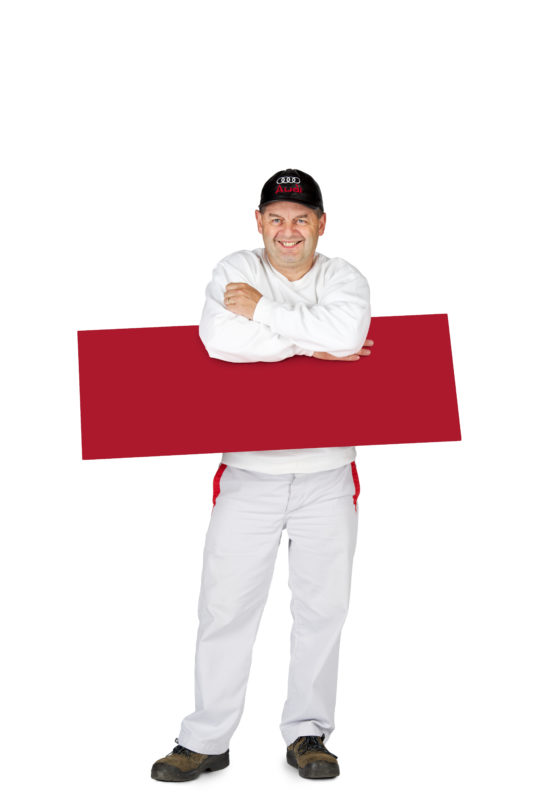 Employees photography: For a personnel campaign of a vehicle manufacturer, employees pose with a red sign against a white background. The photos are full body shots and each person acts differently in front of the camera. Here an employee has clamped his sign under his arms.