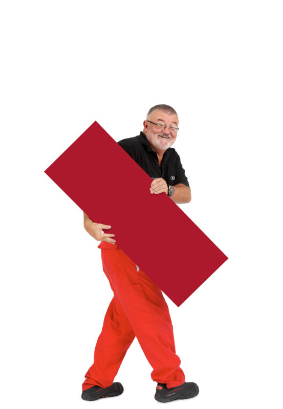 Employees photography: For a personnel campaign of a vehicle manufacturer, employees pose with a red sign against a white background. The photos are full body shots and each person acts differently in front of the camera. Here an employee walks through the picture with the sign.