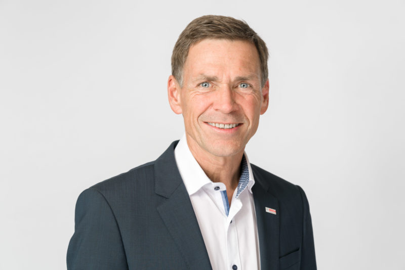 Managerportrait: Manager in landscape format with white shirt and suit, but without tie. The background is light gray and the image has been illuminated with multiple flashes.