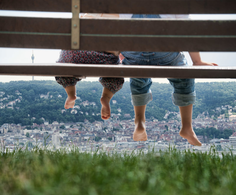 Editorial photography: A little baby and his elder brother sitting outdoors on a bench and look in the Stuttgart basin. In the photo only the feet are shown.