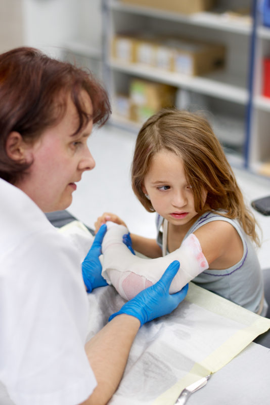 Medizinfotografie: Eine Krankenschwester verbindet einem besorgten Mädchen den Arm um einen Gips anlegen zu können.