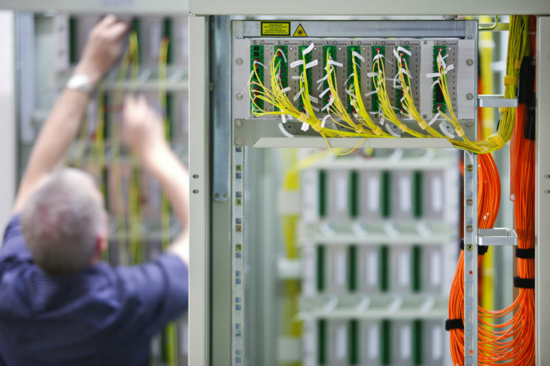 Industriefotografie: Ein Techniker der Deutschen Telekom AG verlegt Glasfaserkabel in einer Vermittlungsstelle.