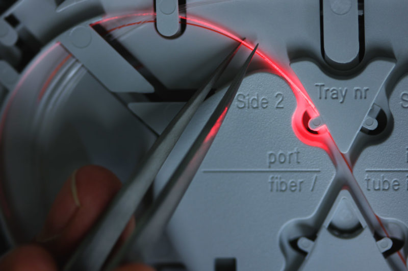 Industriefotografie: Der rote Laserstrahl in einem Glasfaserkabel leuchtet wenn man es krümmt.