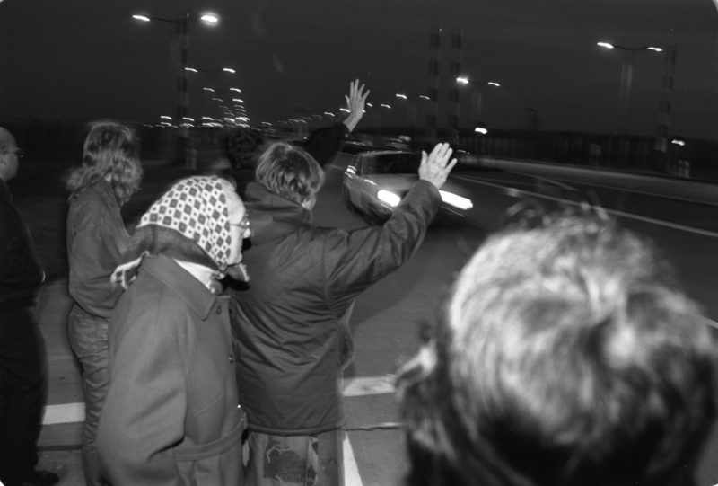 Reportagefotografie DDR Grenzöffnung 1989: Fahrzeuge aus der DDR fahren über die offene Grenze am Grenzübergang Helmstedt/Marienborn und werden von winkenden Westdeutschen begrüßt.