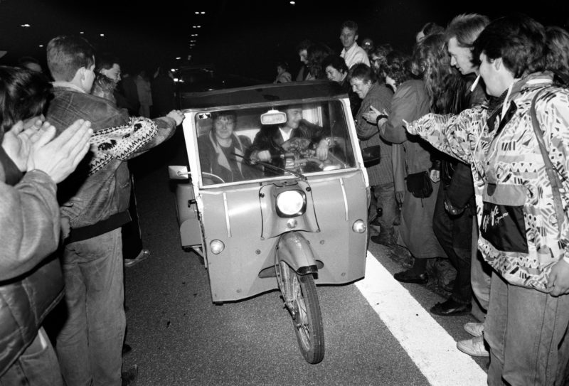 Reportagefotografie DDR Grenzöffnung 1989: Fahrzeuge aus der DDR fahren über die offene Grenze am Grenzübergang Helmstedt/Marienborn und werden von winkenden Westdeutschen begrüßt.