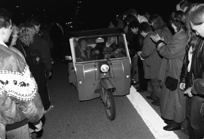 Reportagefotografie DDR Grenzöffnung 1989: Fahrzeuge aus der DDR fahren über die offene Grenze am Grenzübergang Helmstedt/Marienborn und werden von winkenden Westdeutschen begrüßt.